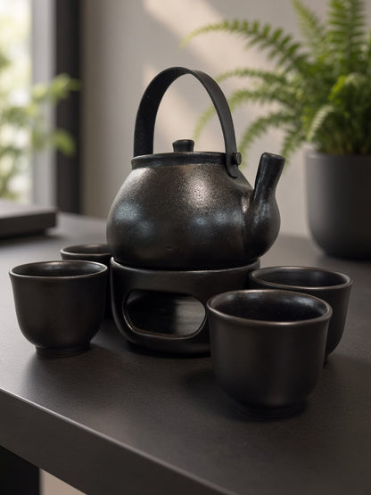 Black pottery teapot on its warming stand with four handleless cups