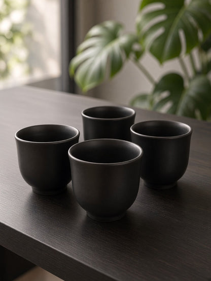 Four handleless matte black pottery cups